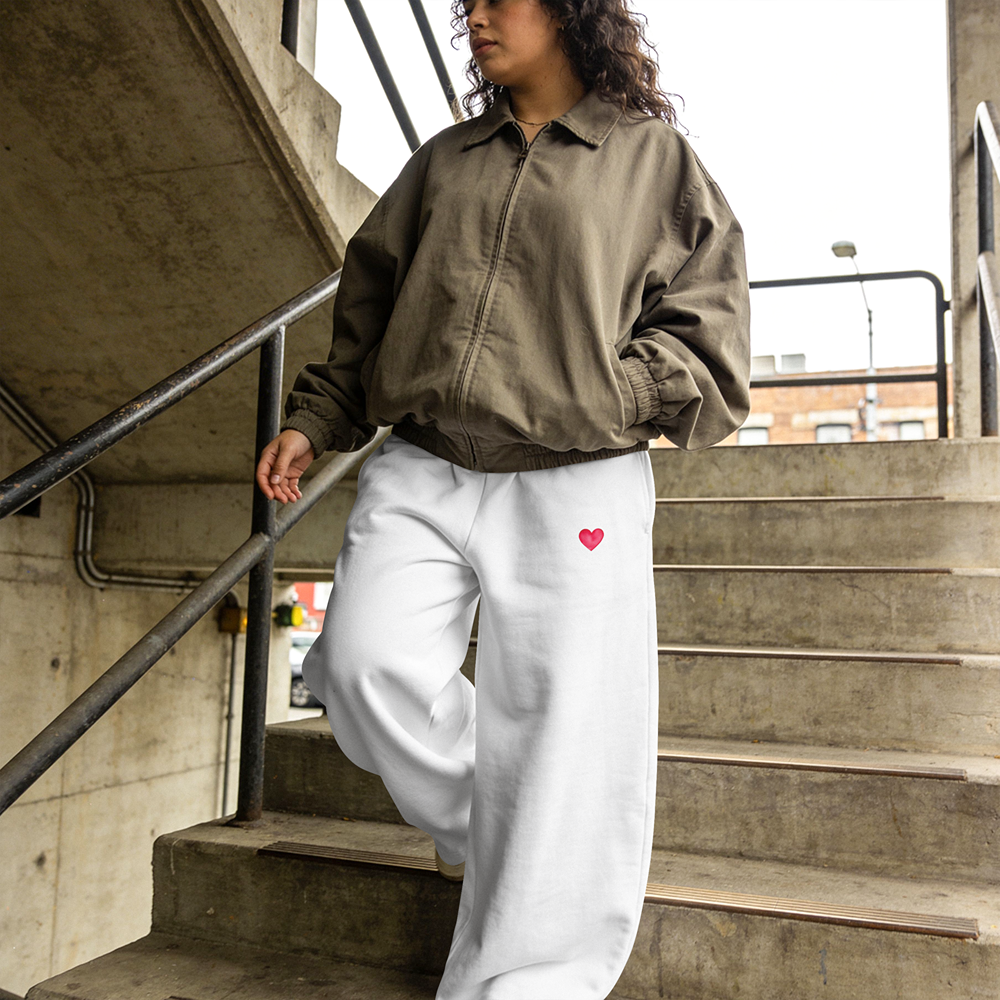 White sweatpants with pink heart detail, styled with olive jacket on urban stairs — streetwear fashion