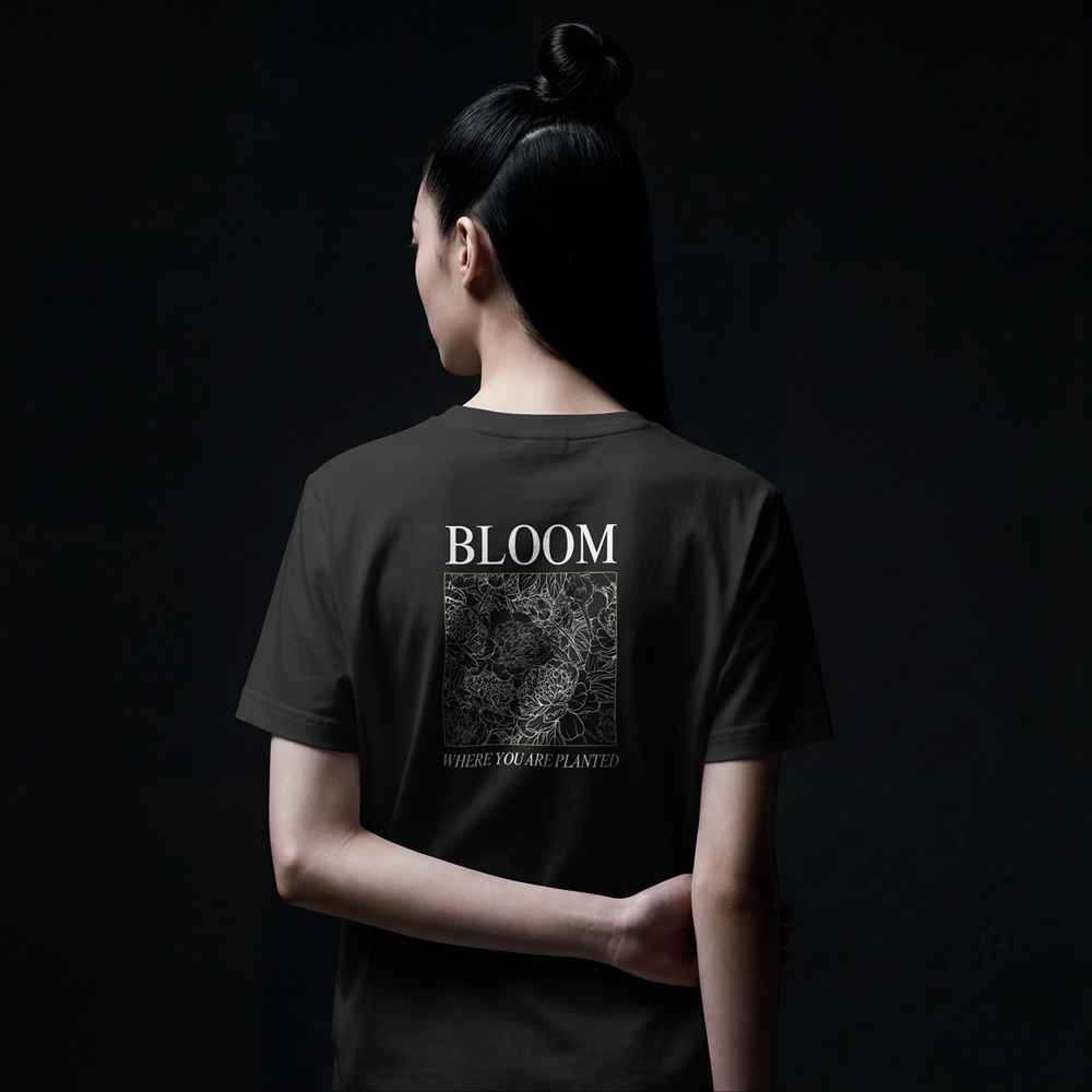 Woman wearing black graphic tee with 'BLOOM WHERE YOU ARE PLANTED' floral design, bold streetwear style
