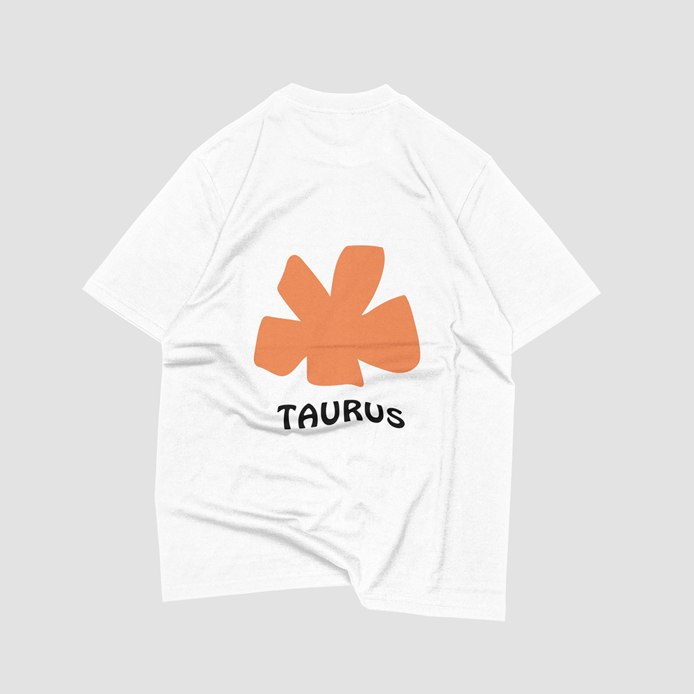 White graphic t-shirt with orange Taurus zodiac symbol and bold text, ideal for streetwear and lifestyle fashion.