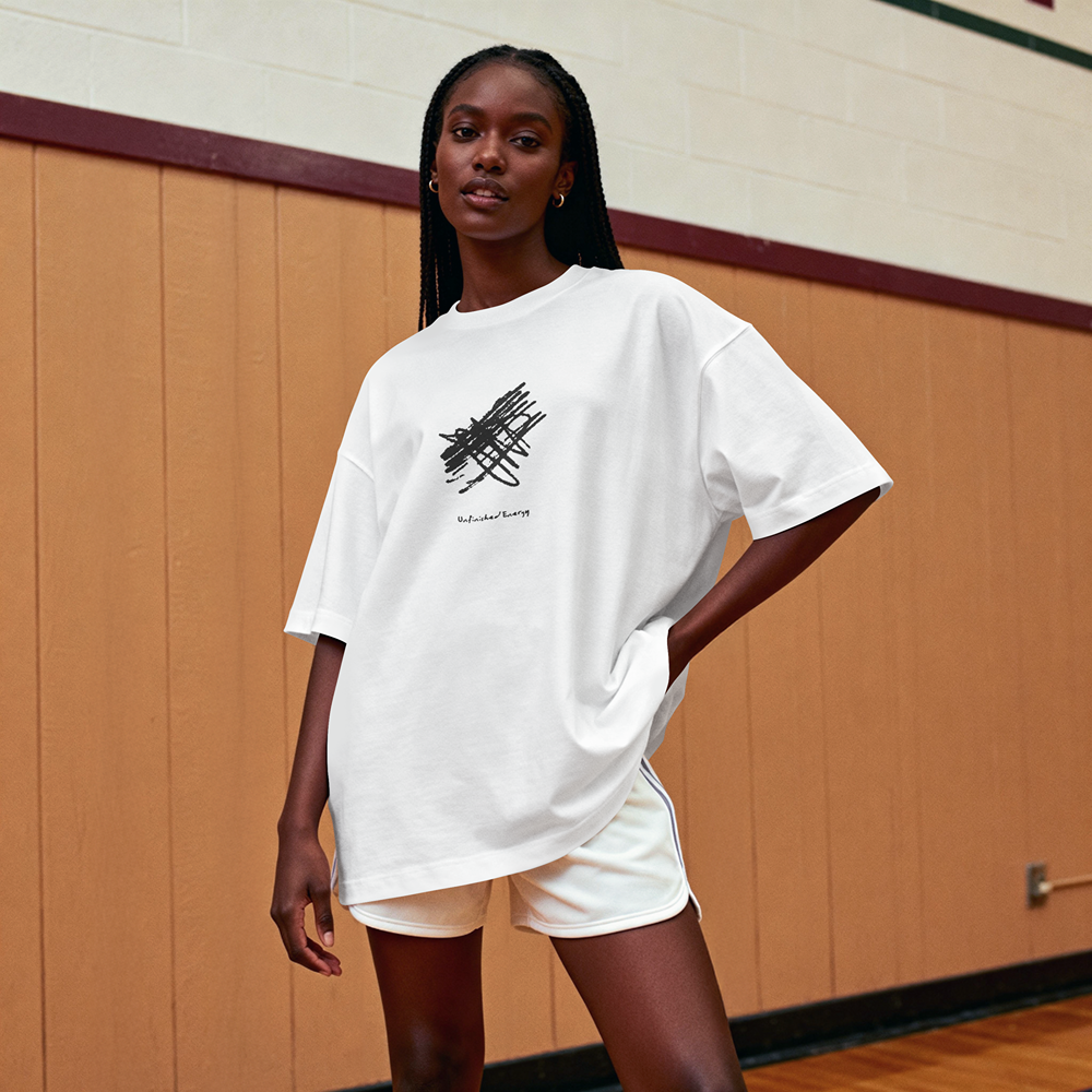 White oversized graphic tee with abstract black scribble print, styled with shorts in gym setting